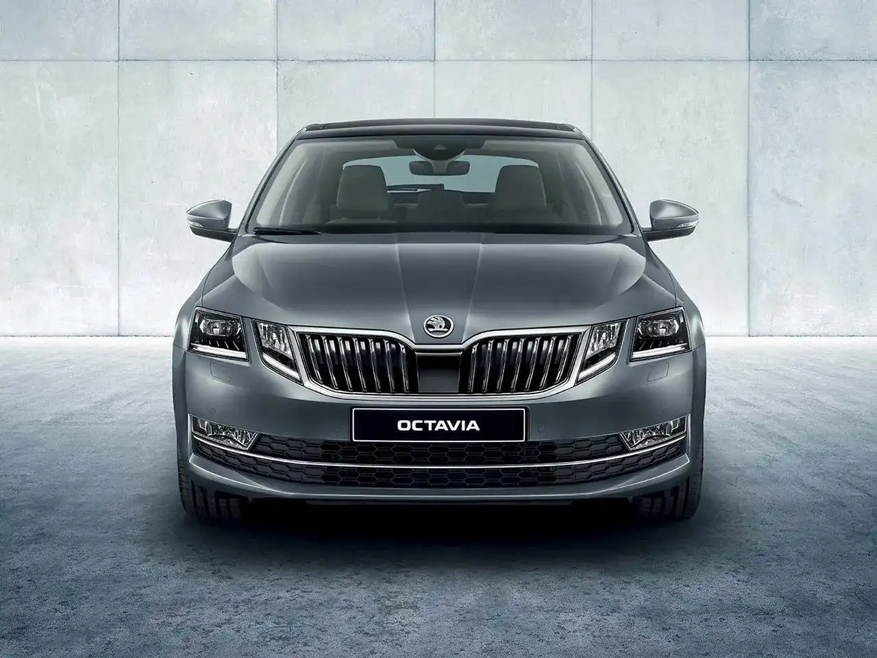 Szary Skoda Octavia sedan z chromowanym grillem i światłami LED, prezentujący się elegancko na tle betonowej ściany.
