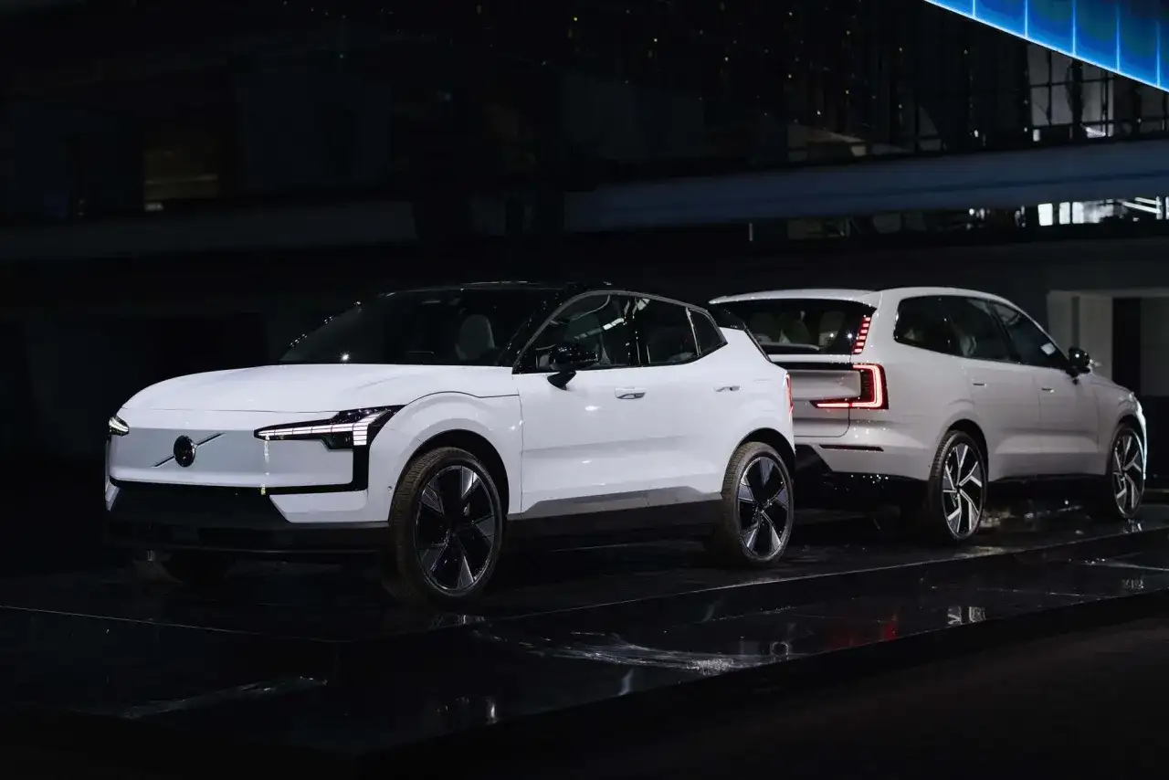 Dwa białe, nowe Volvo na czarnej scenie. Jedno z przodu z charakterystycznymi światłami, drugie z tyłu z nowoczesnymi lampami.