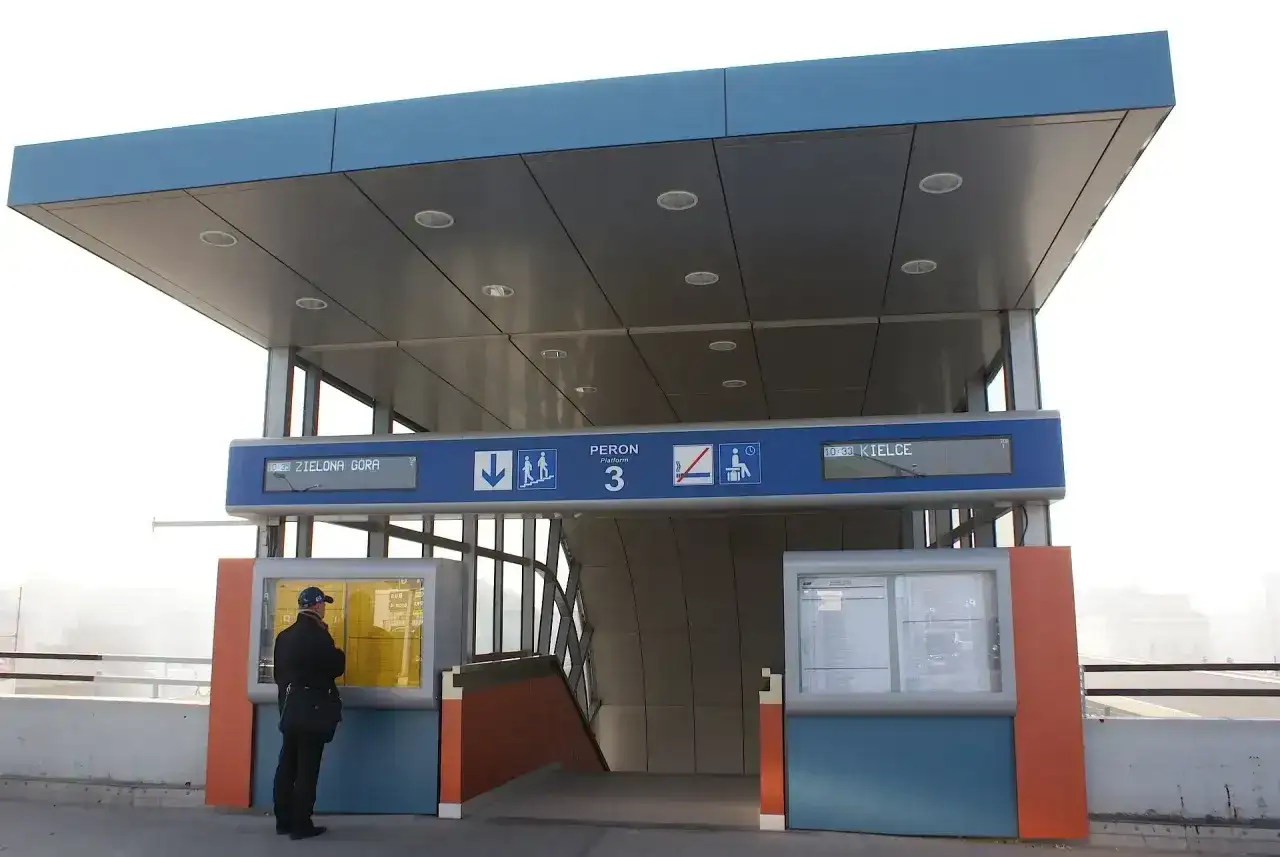 Na dworcu kolejowym mężczyzna sprawdza rozkład jazdy pociągów, szukając połączenia Kraków - Kielce. Peron 3.
