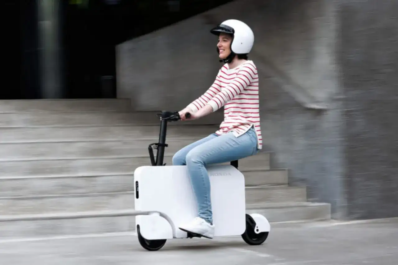 Uśmiechnięta kobieta w kasku jedzie na białym Honda Motocompacto, pokonując miejskie schody.