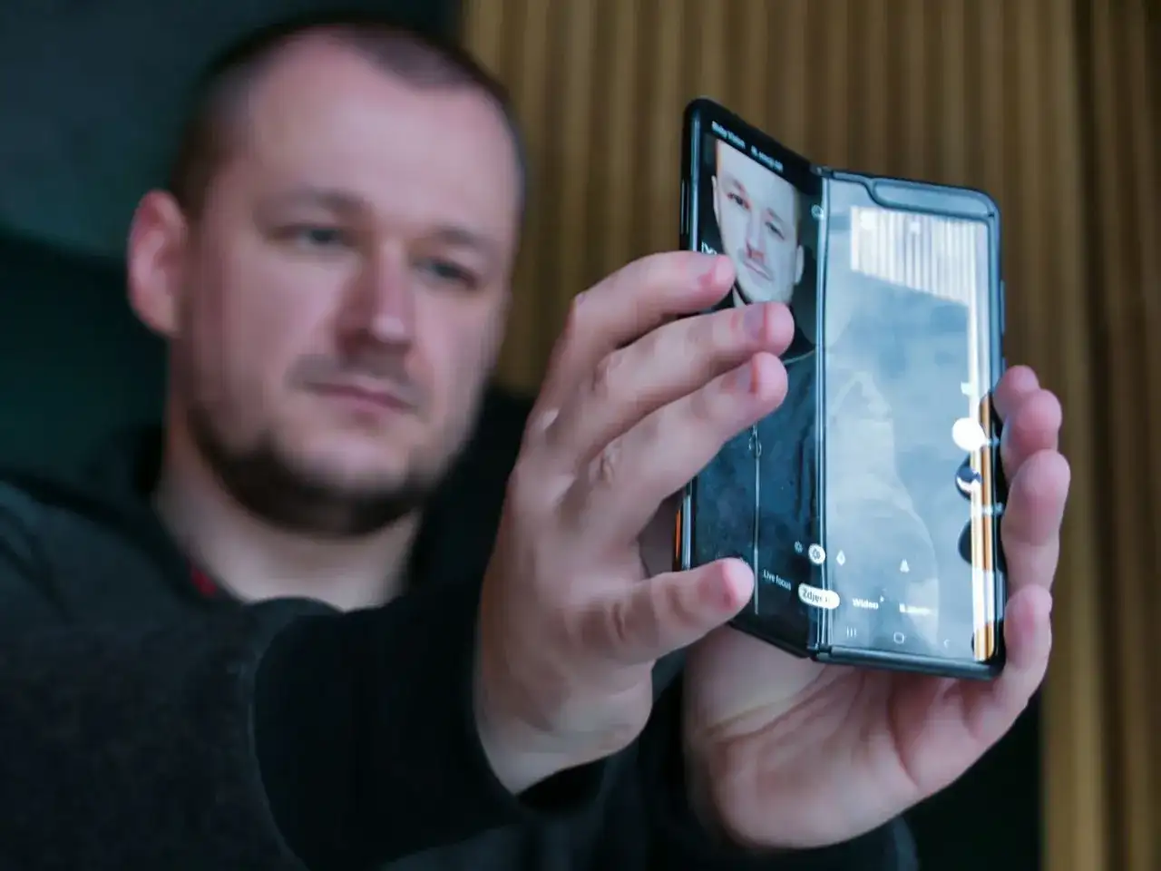 Mężczyzna trzymający składany smartfon, na ekranie którego widać jego twarz.