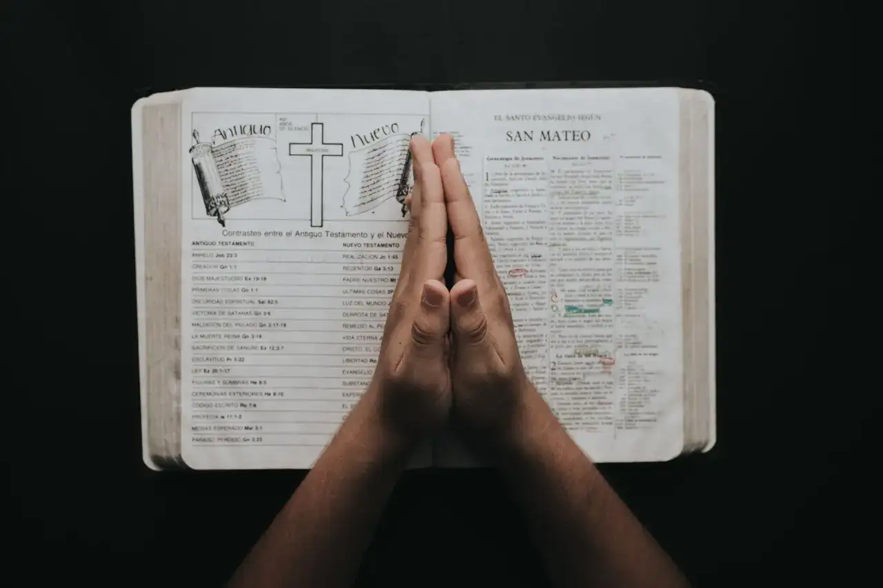 Dłonie złożone do modlitwy nad otwartą Biblią, na stronie z porównaniem Starego i Nowego Testamentu, gdzie wspomniany jest psalm 23.