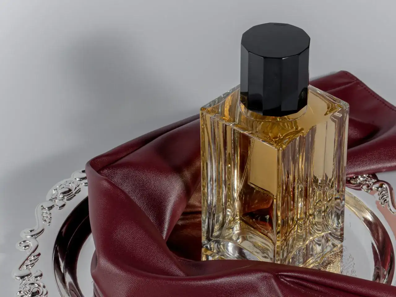 Elegancka butelka perfum na ozdobnej tacy, otulona bordową skórą. To wyjaśnia, dlaczego znana modelka nigdy nie używa tradycyjnych perfum z drogerii.