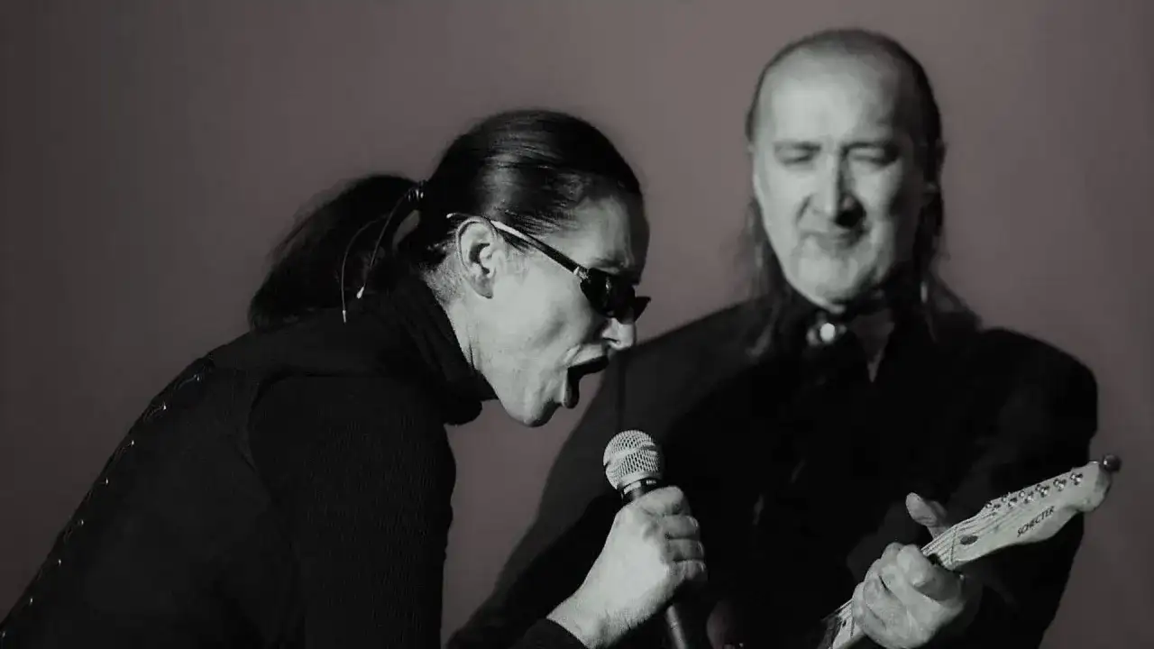 Kora śpiewa do mikrofonu, a obok niej gra na gitarze muzyk. To scena z koncertu, gdzie można usłyszeć maanam piosenki alfabetycznie.