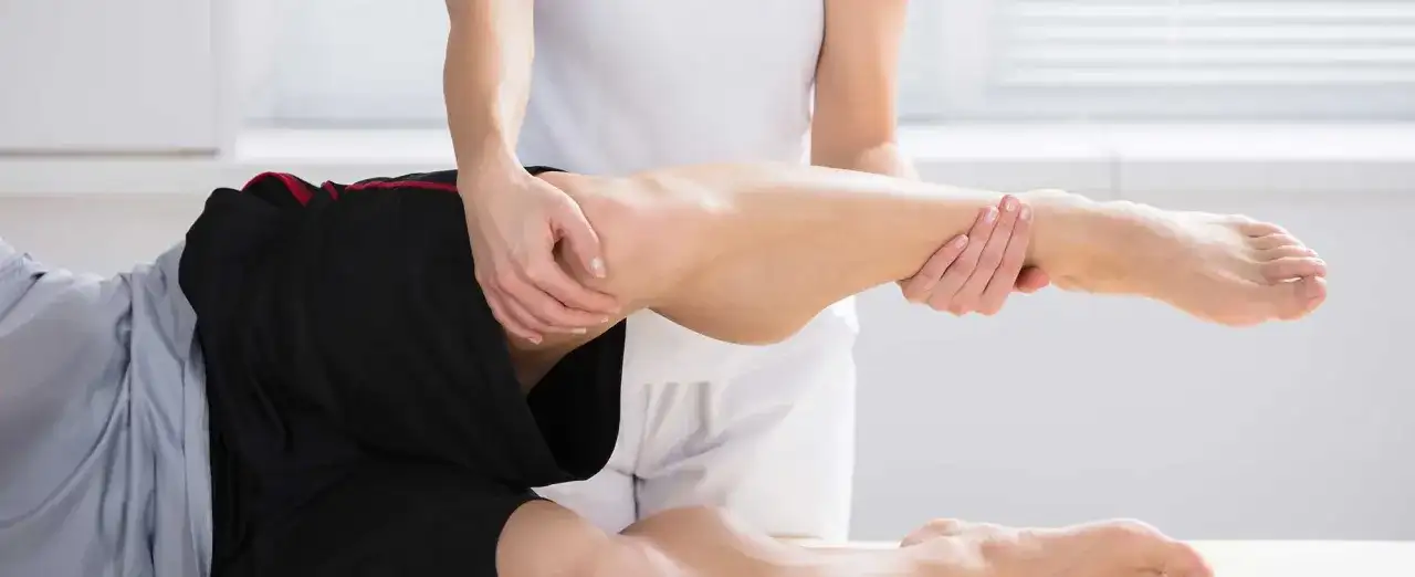 Fizjoterapeuta pomaga pacjentowi z bólem kolca biodrowego, wykonując delikatne ruchy nogą.