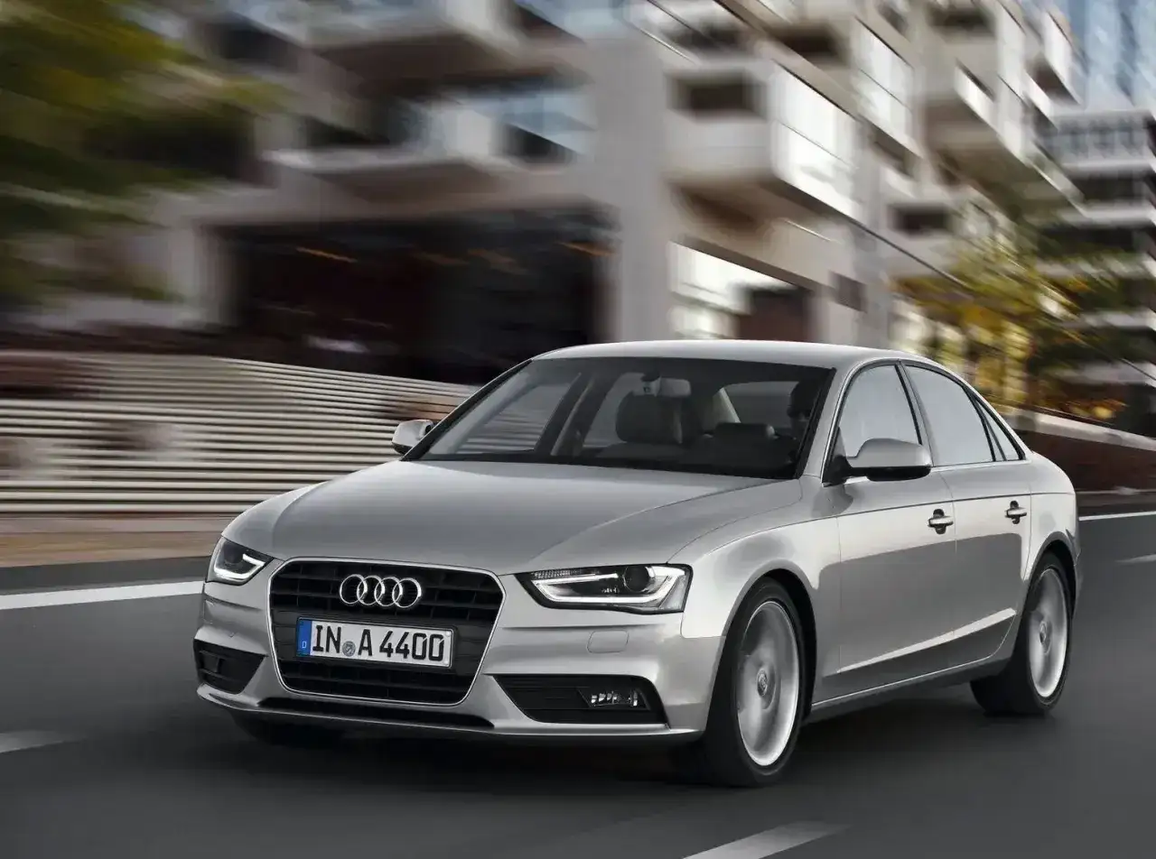 Srebrne Audi A4 B8 pędzi ulicą, rozmywając tło nowoczesnych budynków.