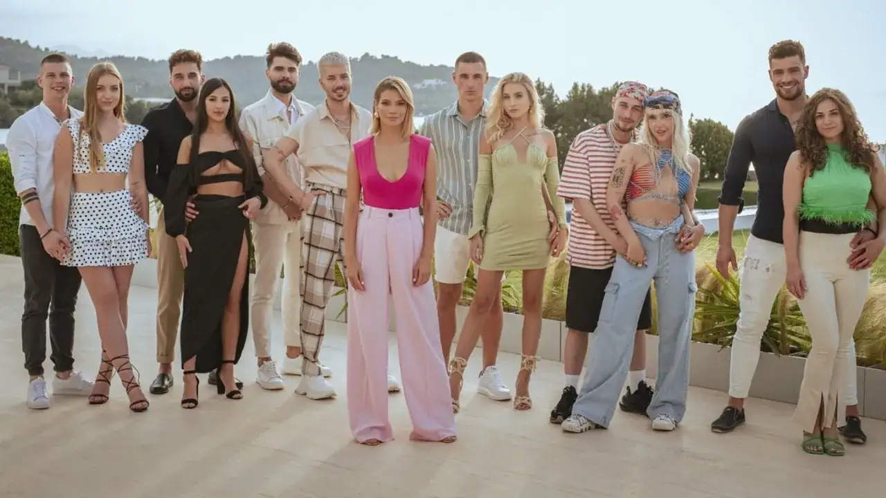 Grupa młodych ludzi pozuje do zdjęcia. Widać ich stroje, uśmiechy, ale czego nie widać w kamerach podczas nagrań reality show?