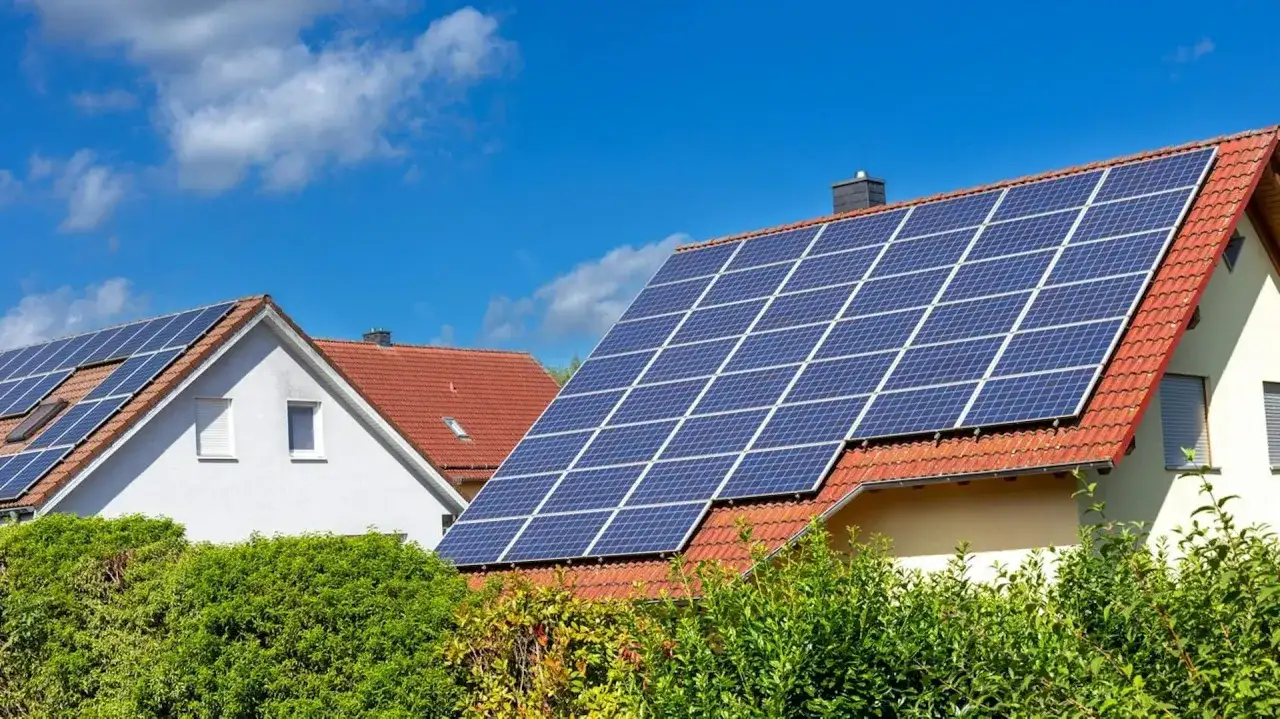 Domy z fotowoltaiką na dachu, zbierające energię słoneczną. Zielone krzewy przed budynkami.