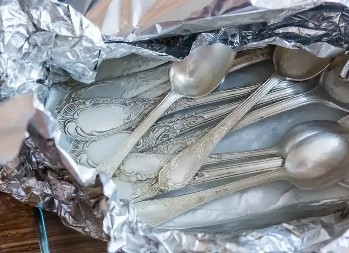 Stare, ozdobne łyżki i widelce owinięte w folię aluminiową, gotowe do czyszczenia srebra.