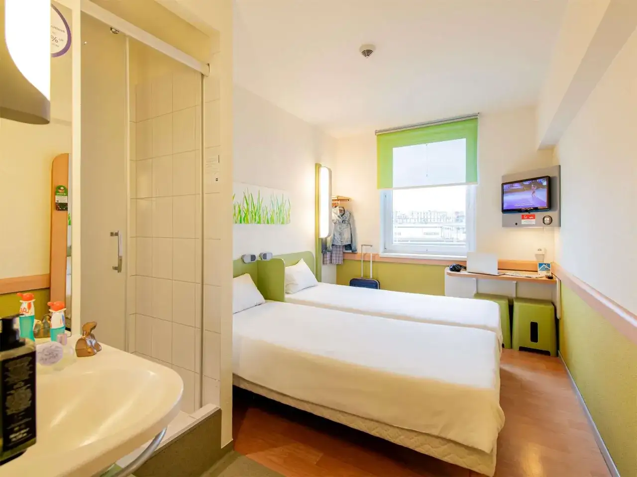 Pokój w hotelu Ibis z dwoma łóżkami, łazienką, biurkiem z laptopem i telewizorem.