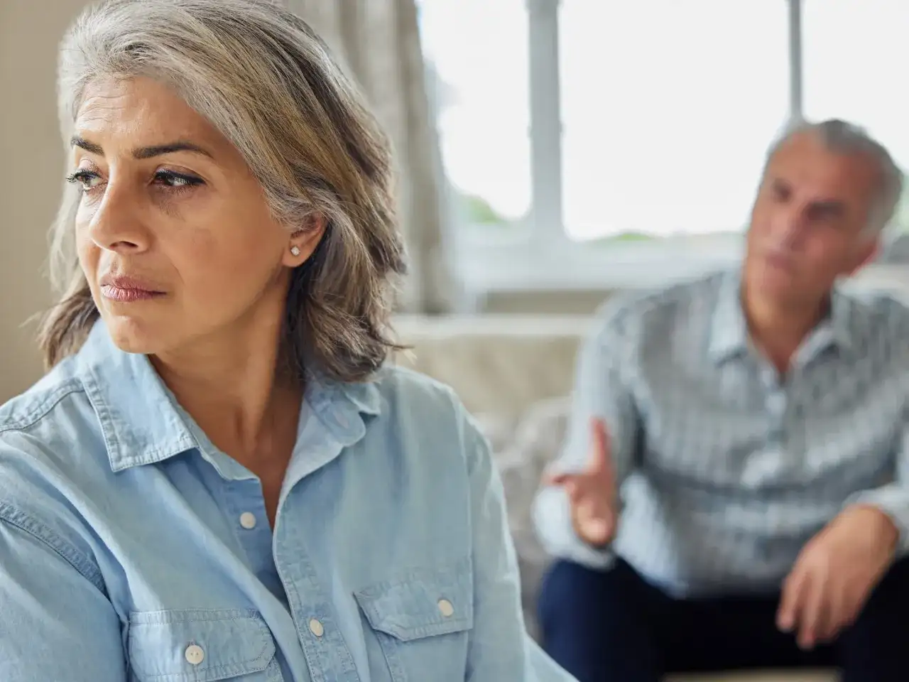 Een vrouw kijkt weg tijdens een gesprek, de man op de achtergrond gebaart. Dit beeld roept de vraag op: wanneer heeft relatietherapie geen zin?