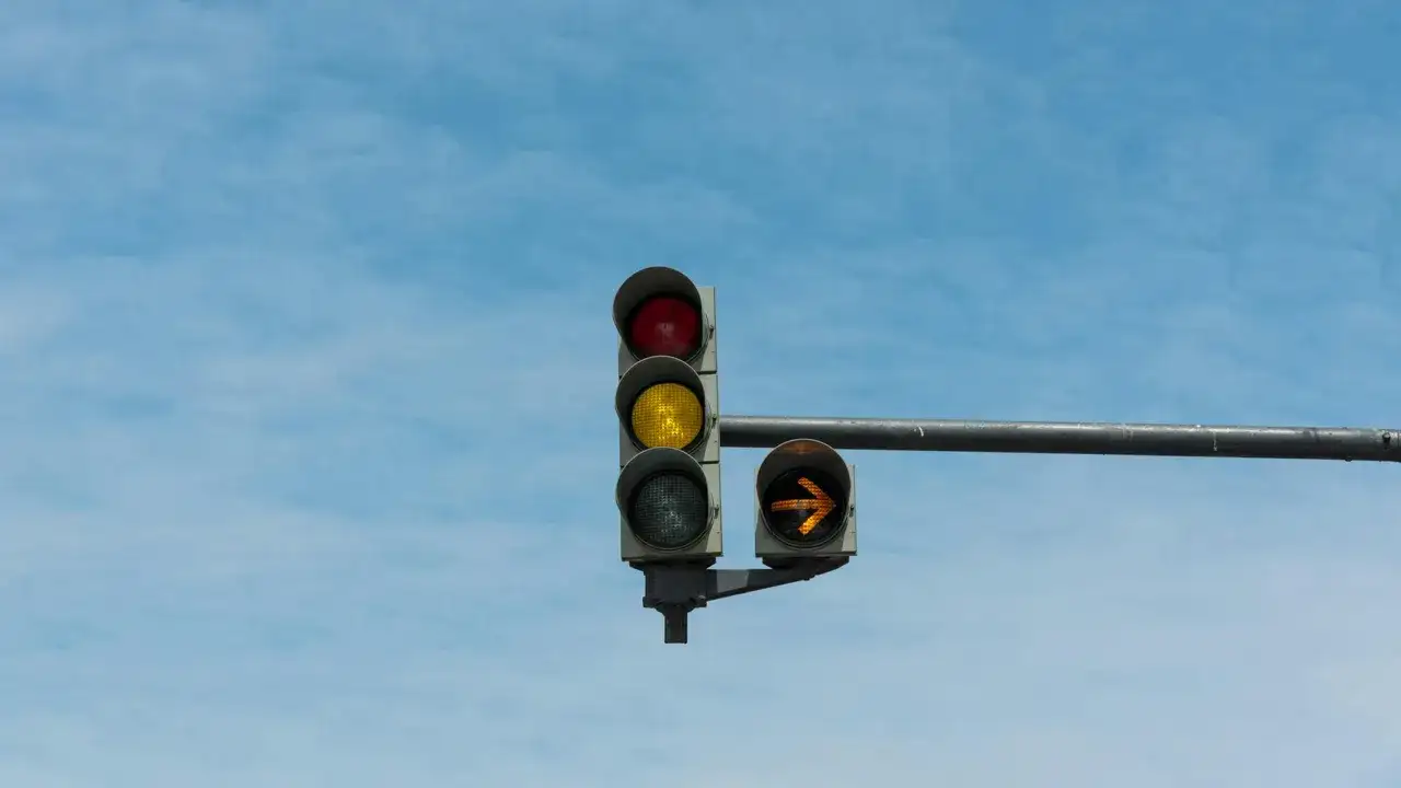Feu de circulation avec le rouge allumé, le jaune clignotant en bas, et une flèche orange clignotant à droite.