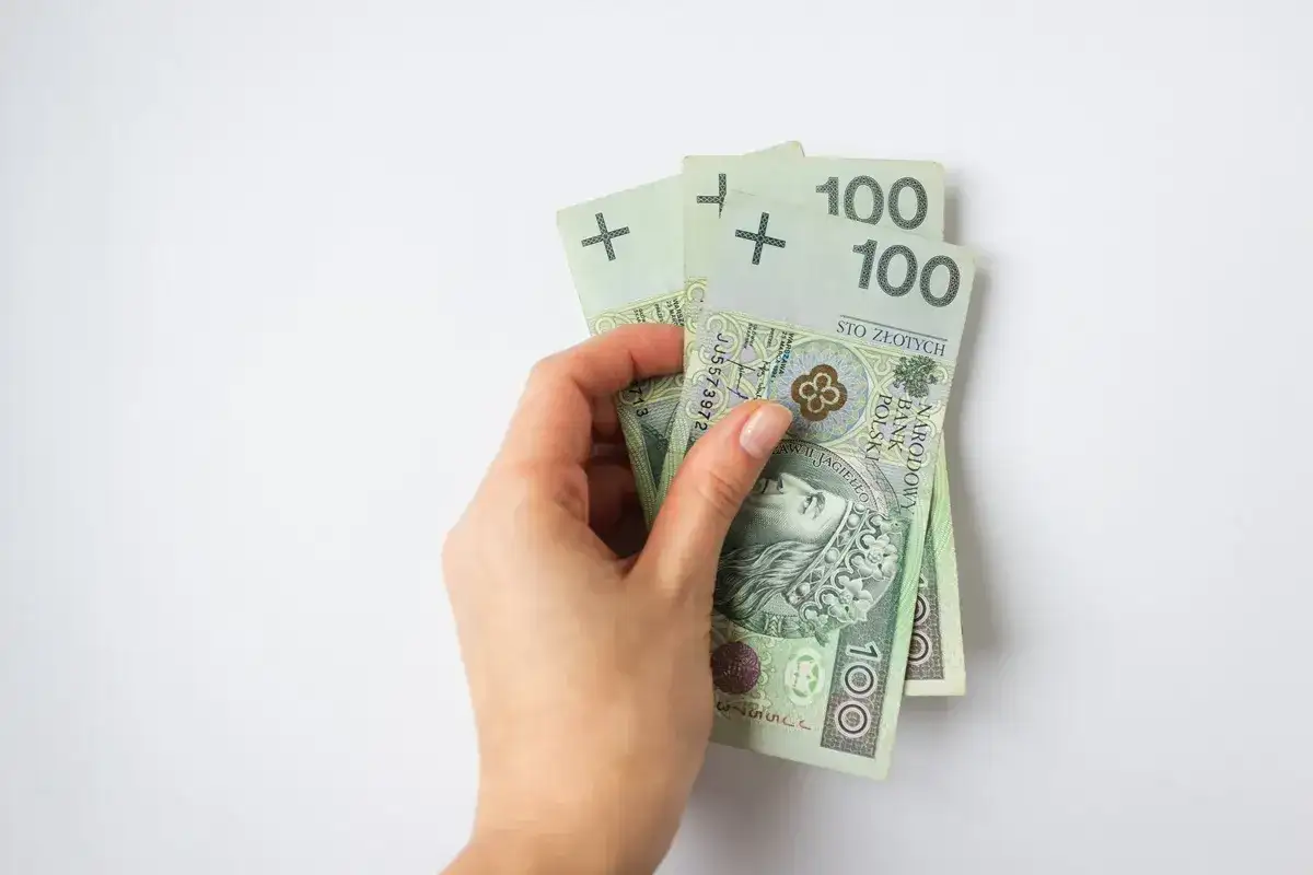 Dłoń trzyma trzy banknoty po 100 złotych. To dobry start do oszczędzania.