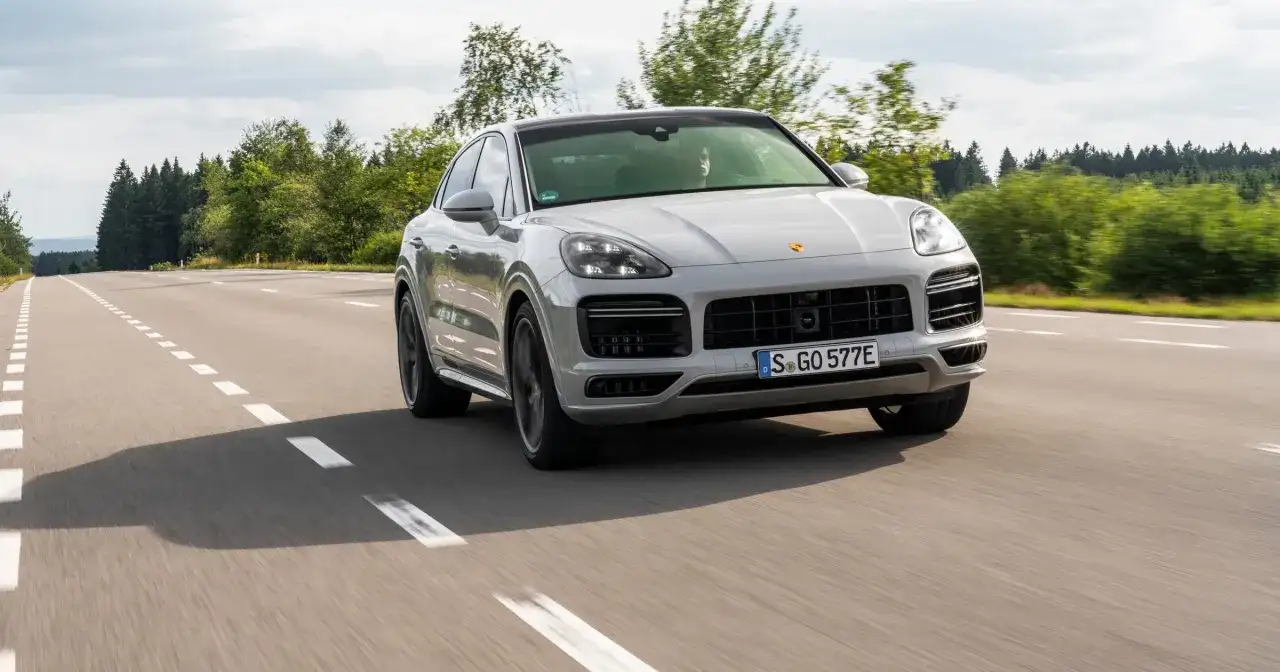 Srebrny Porsche Cayenne 2025 sunie po asfaltowej drodze, otoczony zielenią lasów.
