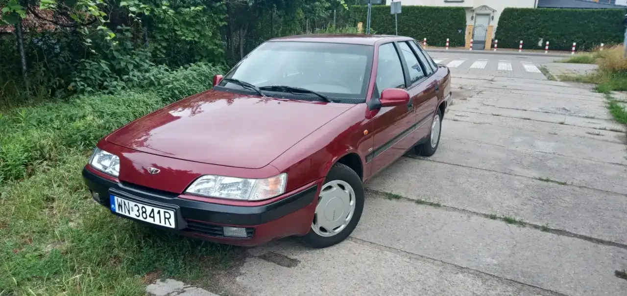 Czerwony Daewoo Espero z tablicą rejestracyjną WN 3841R stoi na betonowej drodze obok zielonego trawnika.