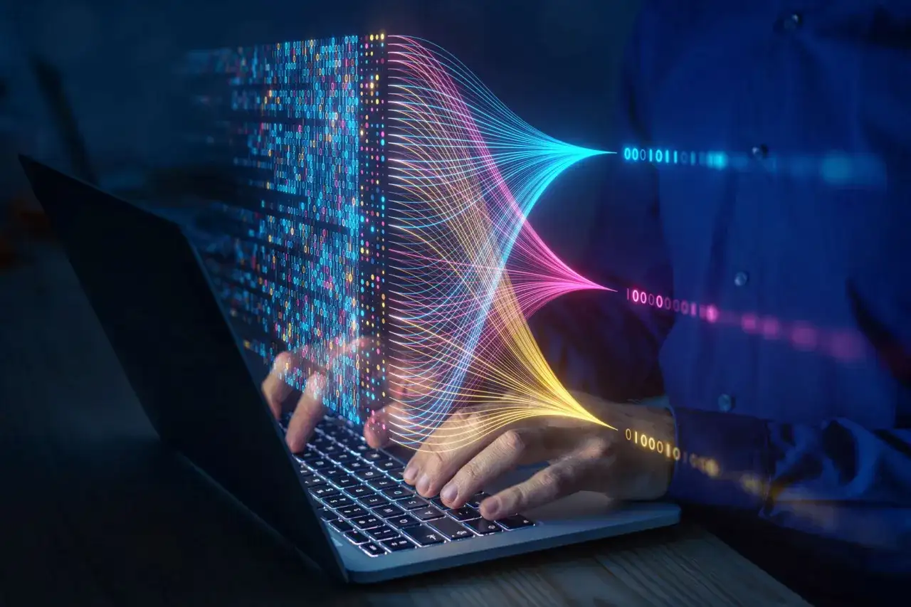 Ręce na klawiaturze laptopa, wizualizacja danych w postaci kolorowych linii i kodu binarnego. Przyszłość elektrotechniki w cyfrowym świecie.