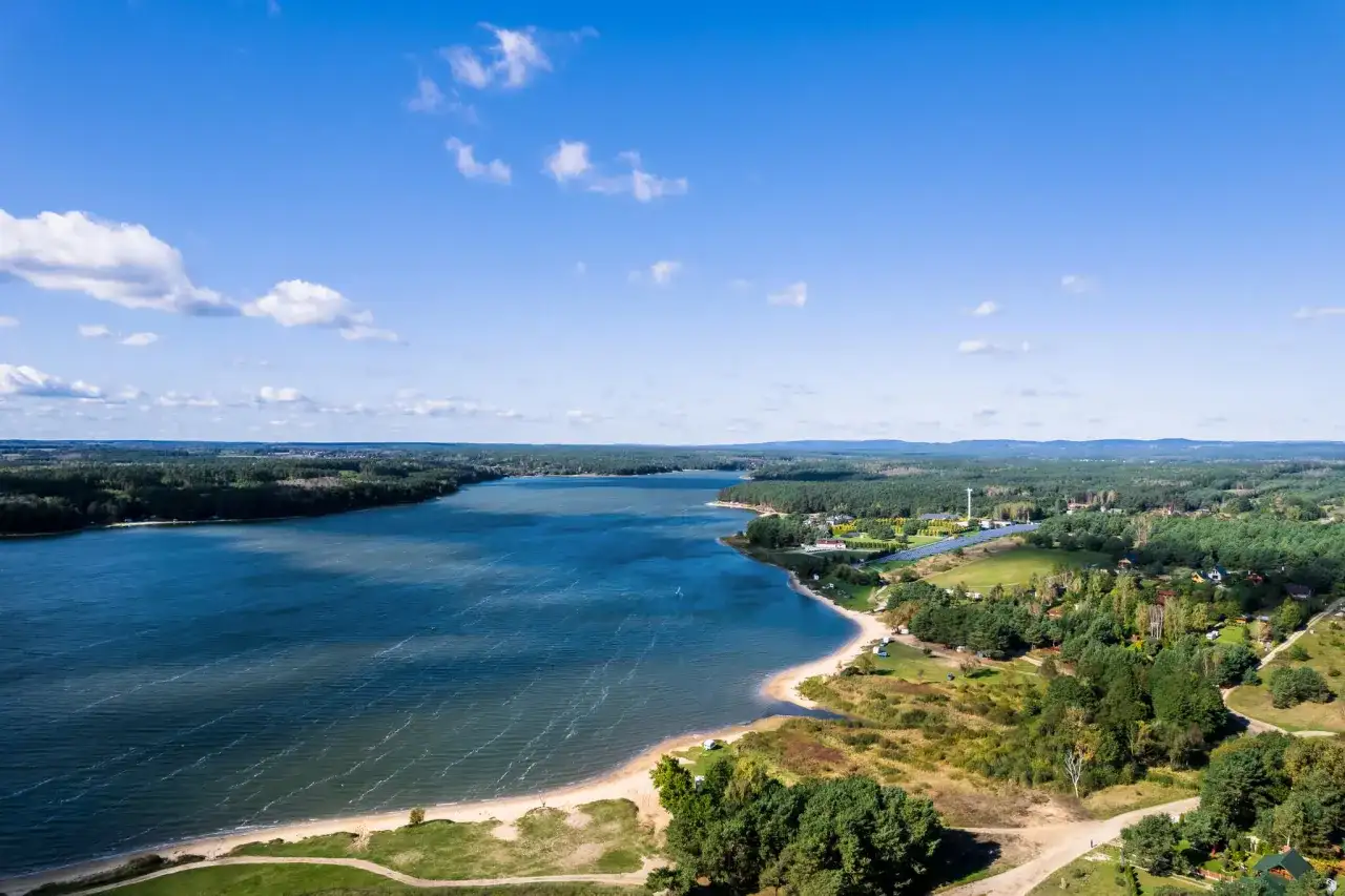 Malownicze jezioro Chańcza otoczone lasami, z piaszczystą plażą i zabudowaniami w tle.