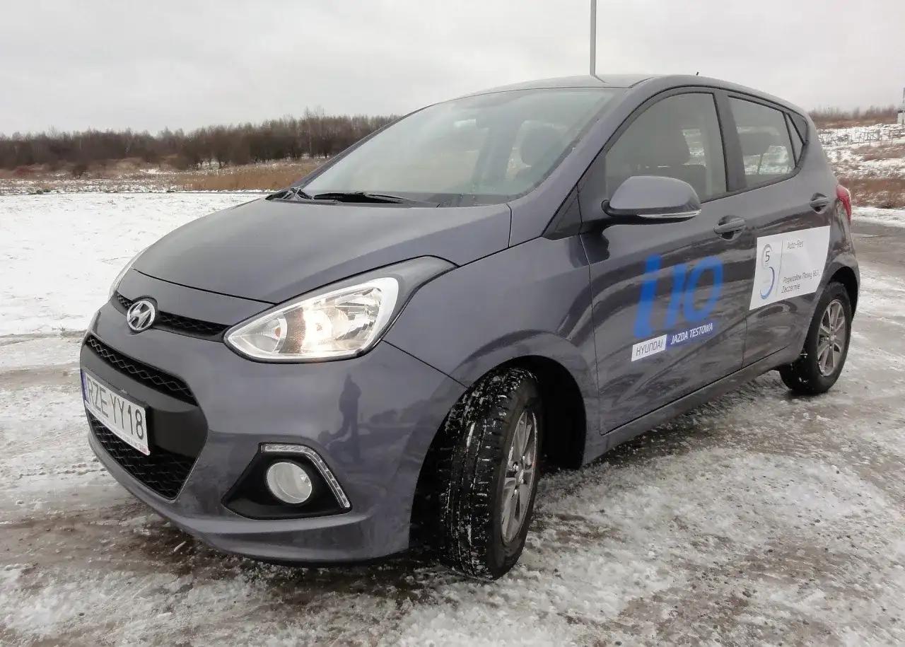 Szary Hyundai i10 na zimowych oponach, gotowy do jazdy testowej po zaśnieżonym terenie.