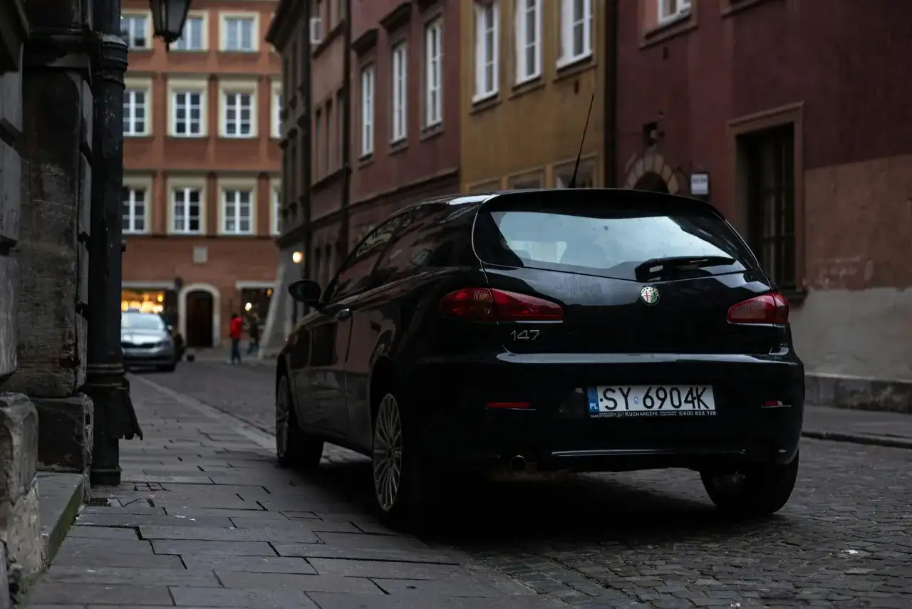 Czarny Alfa Romeo 147 na wąskiej uliczce. Czyj to numer rejestracyjny samochodu? SY 6904K.
