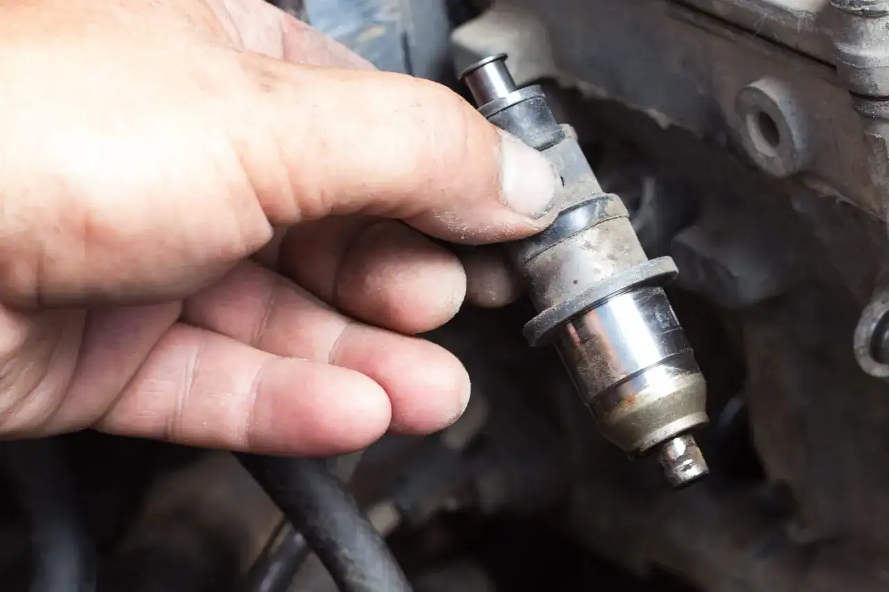 Main d'un mécanicien tenant un injecteur diesel sale. Le prix de la réparation d'injecteur diesel peut varier.