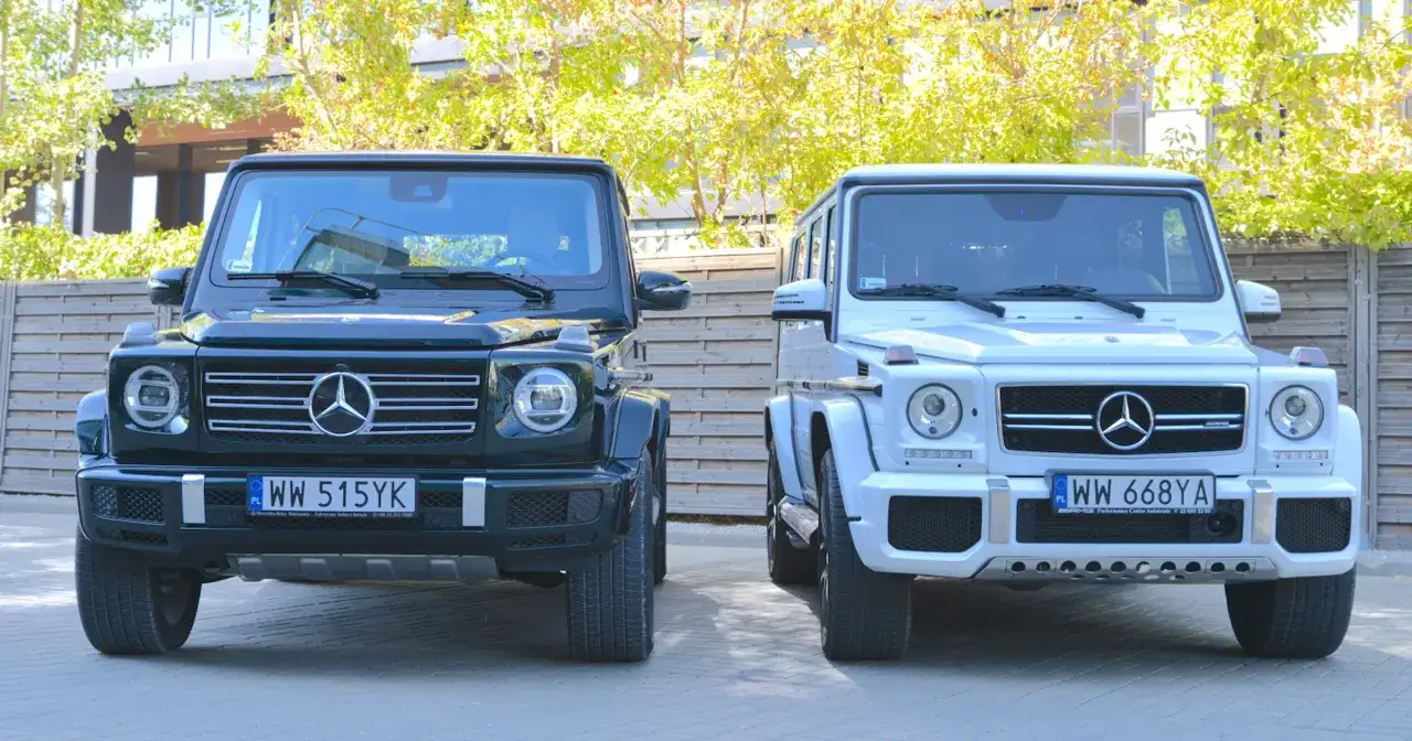 Dwa luksusowe Mercedesy klasy G, czyli gelendy, stoją obok siebie. Jedna jest ciemnozielona, druga biała.