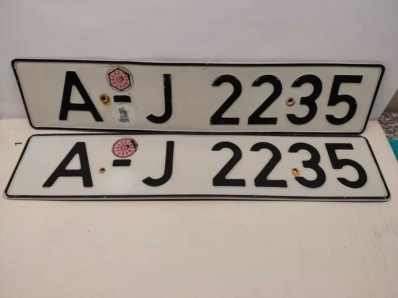 Dwie białe tablice rejestracyjne z czarnymi znakami "AJ 2235". Na górnej tablicy widoczna naklejka z numerem "11" w okręgu. To typowe niemieckie tablice rejestracyjne.