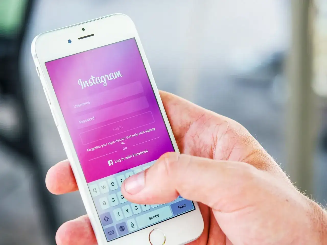 Dłoń trzyma smartfon z ekranem logowania Instagram. Widoczna opcja "Zapomniane dane logowania?" podpowiada, jak odzyskać hasło na Instagramie.