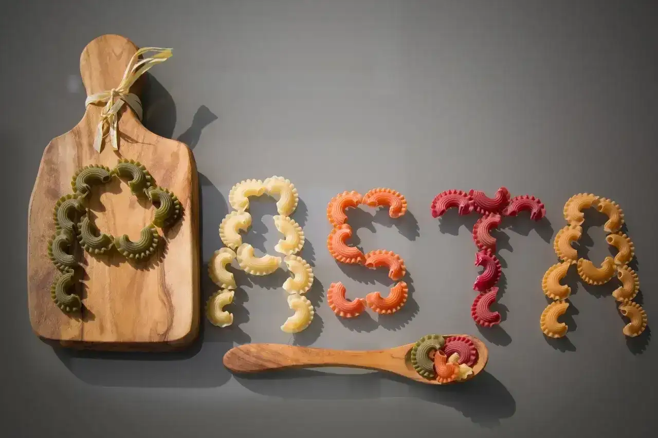 Kolorowy makaron ułożony w napis "PASTA". Kto wymyślił makaron? Może ten, kto ułożył te pyszne kształty na desce i łyżce.