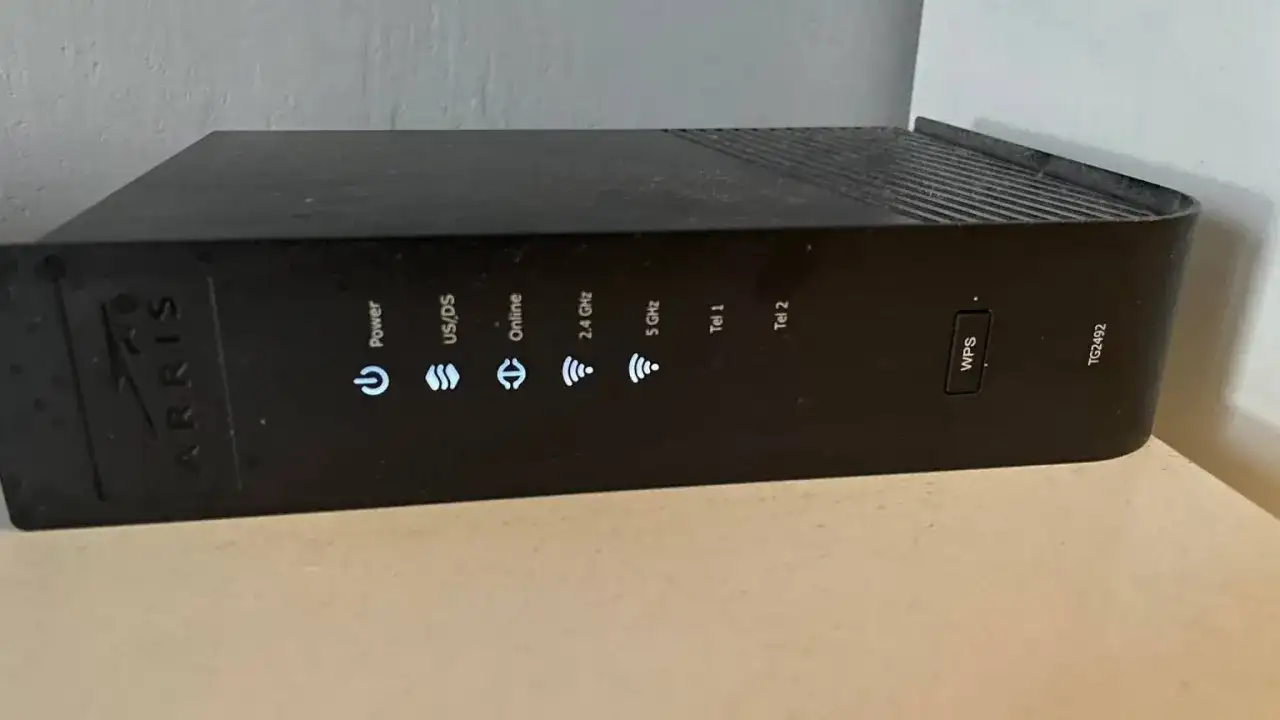 Czarny router Arris TG2492 z widocznym przyciskiem WPS i wskaźnikami statusu: Power, US/DS, Online, 2.4 GHz, 5 GHz, Tel 1, Tel 2.