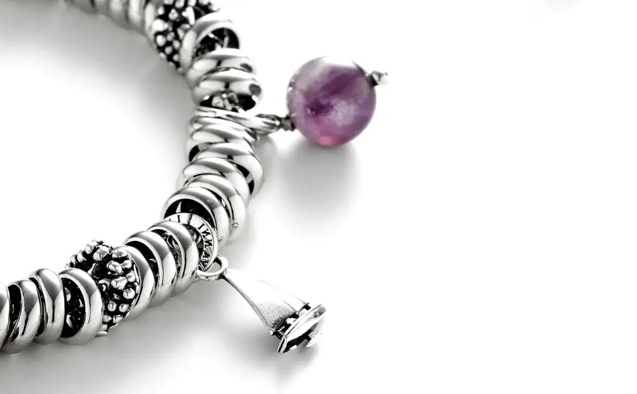 Pulsera de plata con charms, destacando una cuenta de amatista púrpura y un charm en forma de campana.