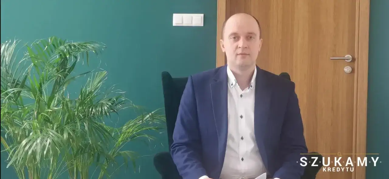 Mężczyzna w garniturze siedzi w fotelu obok rośliny.