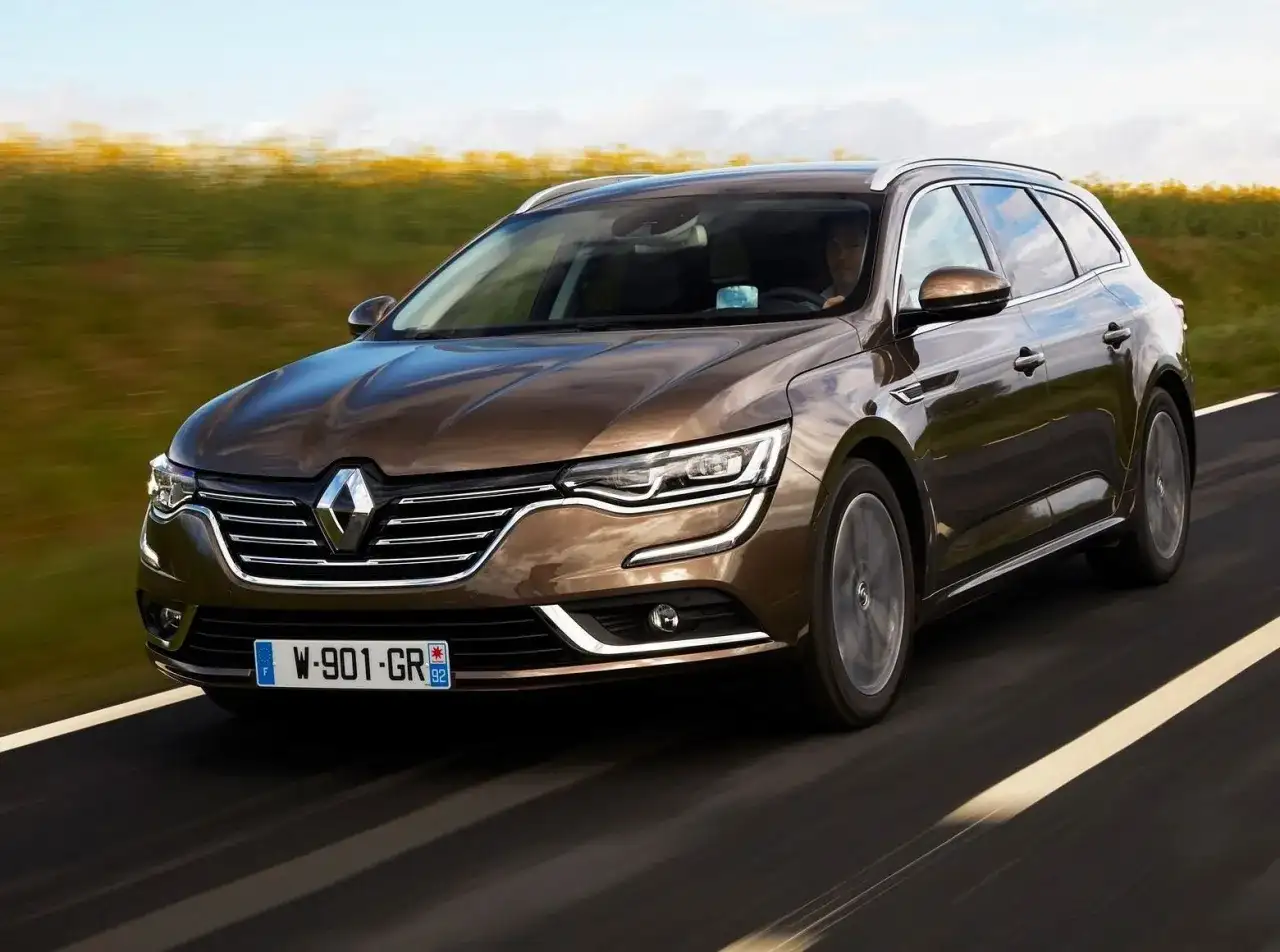 Brązowe renault talisman kombi pędzi po drodze, mijając pola.
