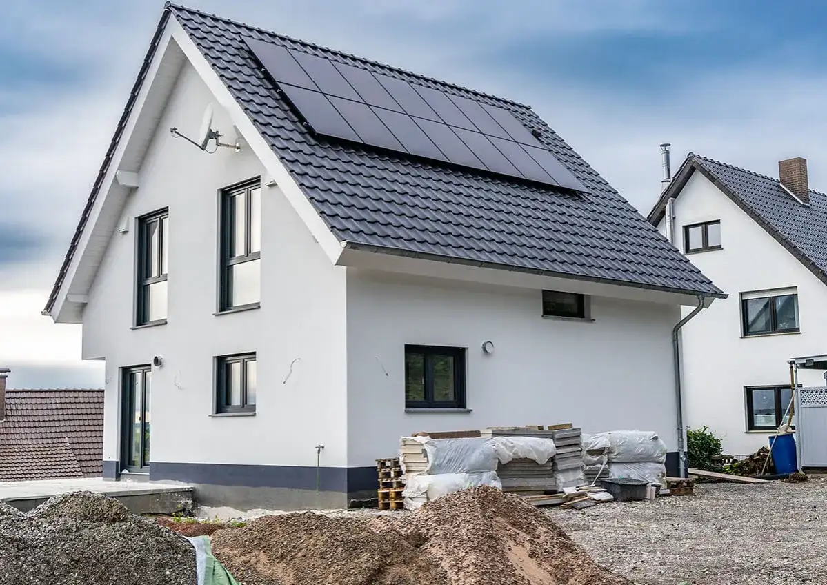 Nowy dom z panelami słonecznymi na dachu, w trakcie rozbudowy. Wokół materiały budowlane.