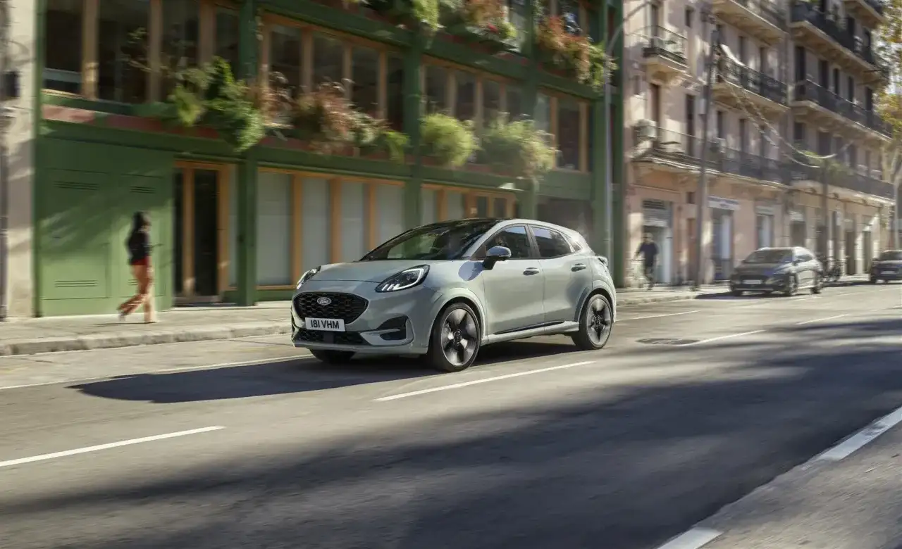 Jasnoszary Ford Puma jedzie ulicą miasta. Sprawdź aktualną ford puma cena i możliwości tego stylowego SUV-a.