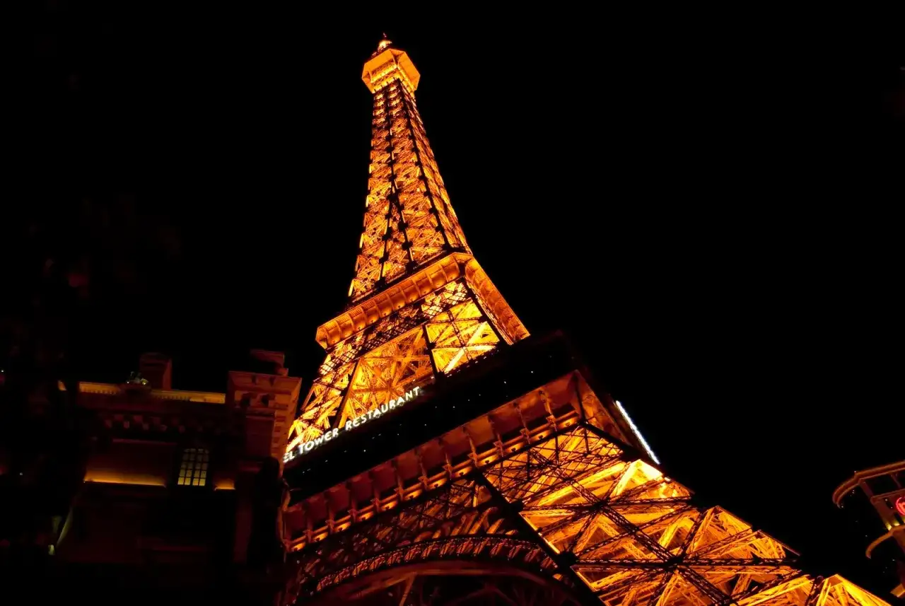 Wieża Eiffla nocą, oświetlona na pomarańczowo. Jej imponująca wysokość robi wrażenie, a napis "Eiffel Tower Restaurant" dodaje uroku.
