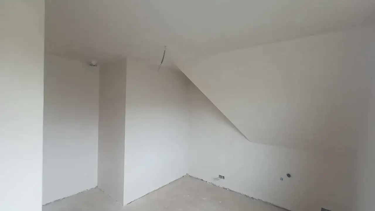 Wnętrze pokoju ze skośnym sufitem, ściany pokryte tynkiem gipsowym bez gładzi, gotowe do malowania.