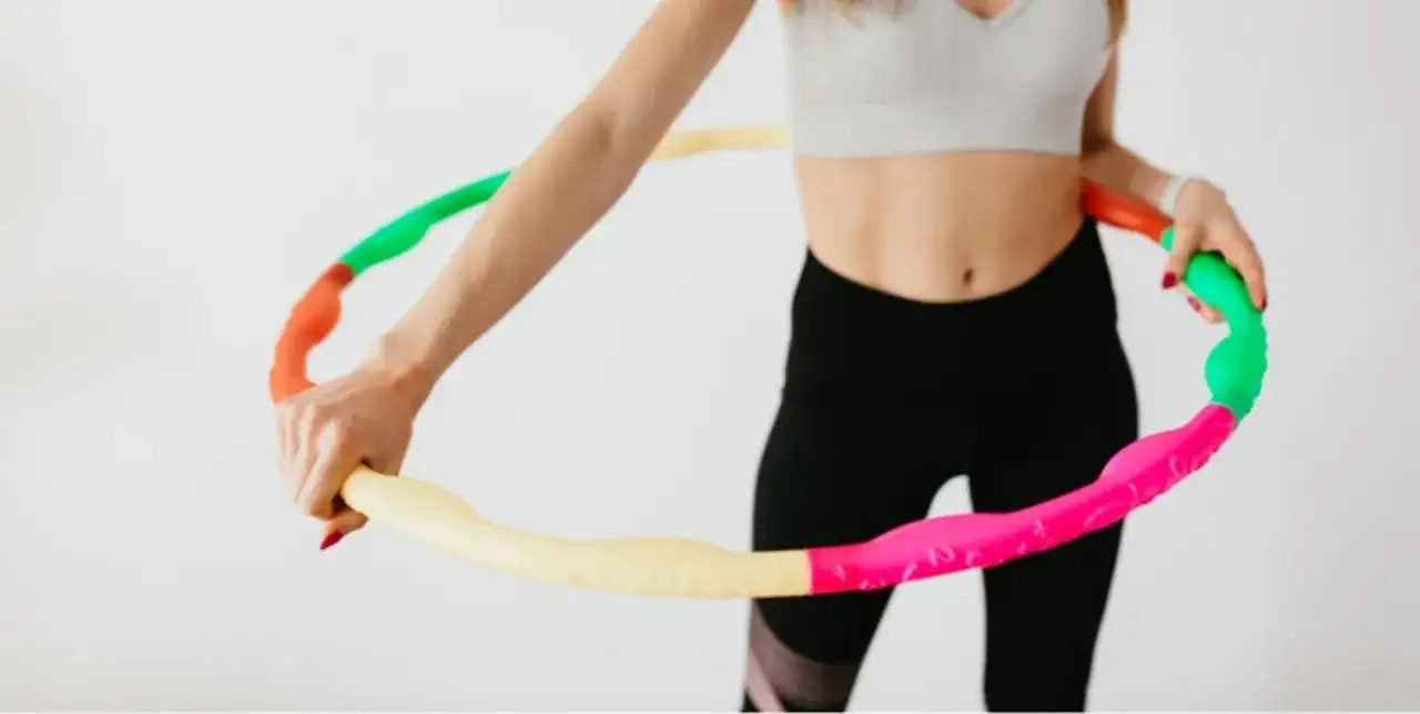Kobieta w sportowym stroju trzyma kolorową obręcz hula hop. Czy hula hop jest szkodliwe? Nie, to świetna zabawa i trening!