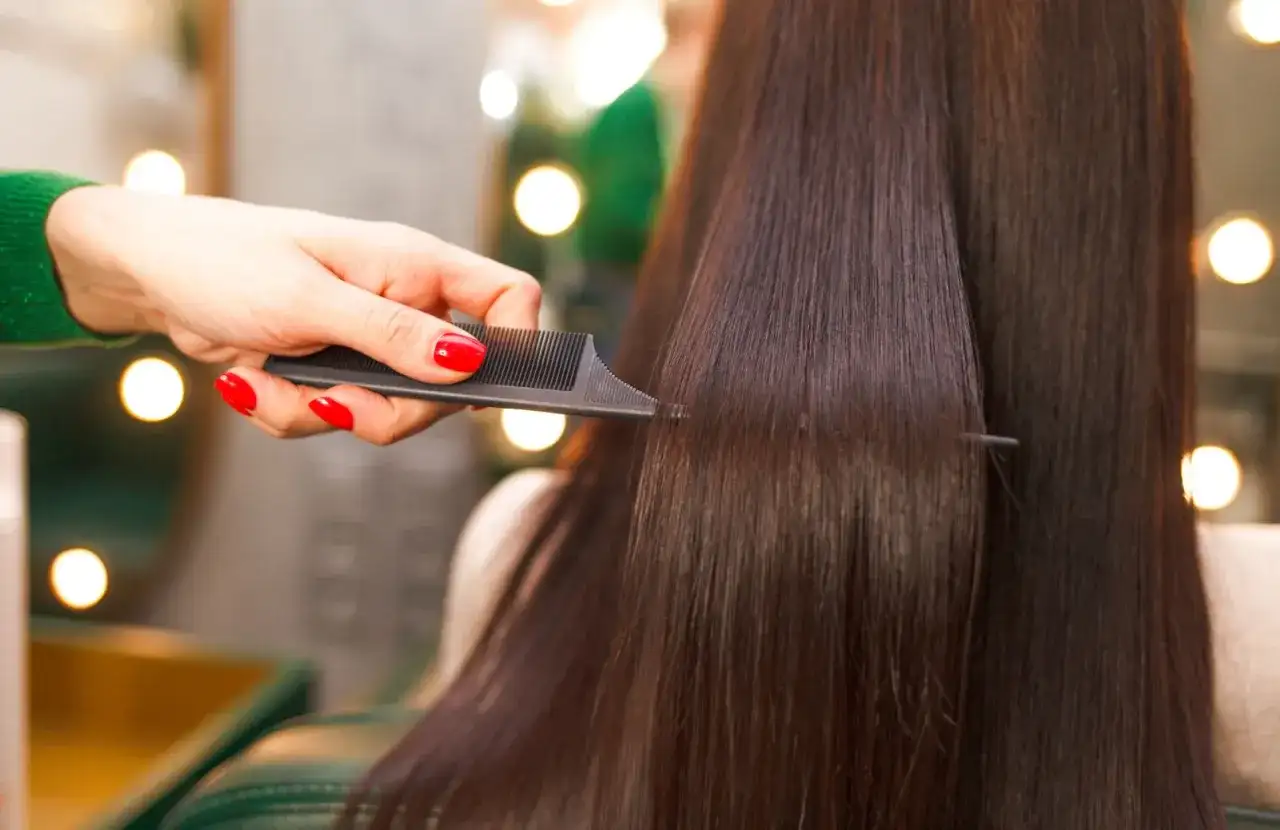 Mano con unghie rosse pettina capelli lisci e scuri, creando un look impeccabile.