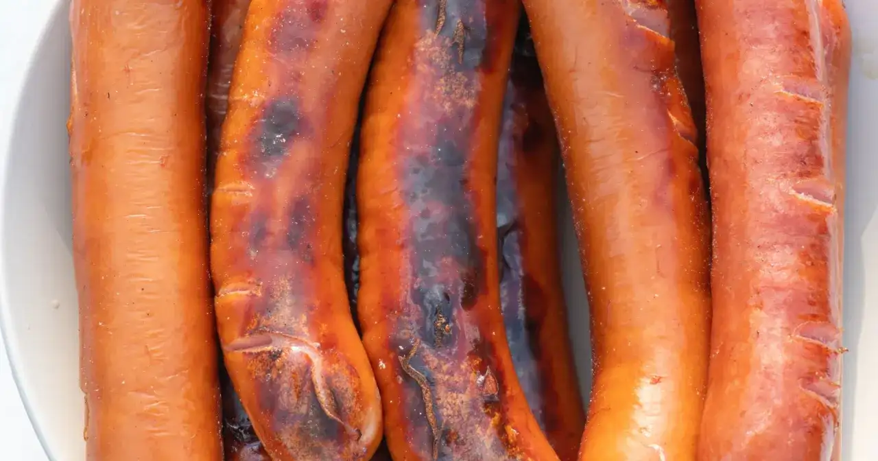 Zbliżenie na kilka grillowanych kiełbasek, niektóre lekko przypalone.