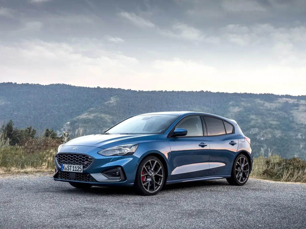 Niebieski Ford Focus MK3 ST na tle gór. Zwróć uwagę na sportowe felgi i opony, które podkreślają jego dynamikę.