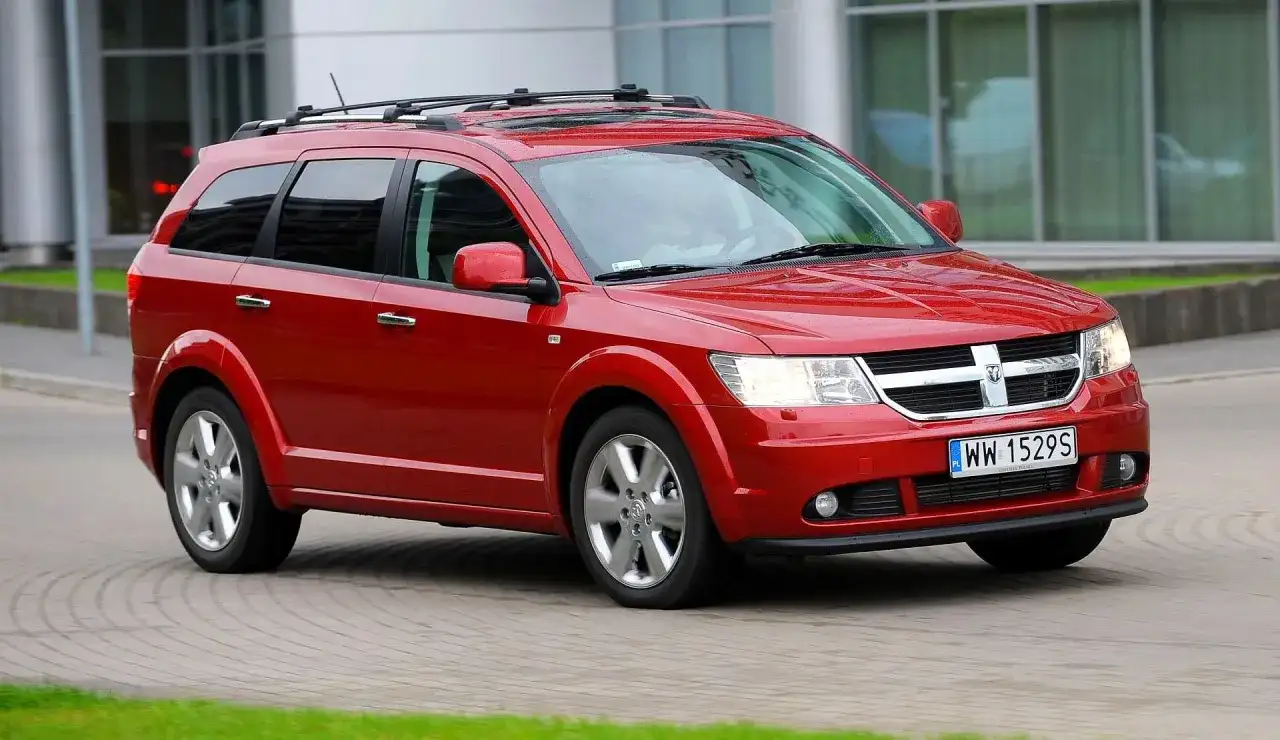 Czerwony Dodge Journey 3.6 z relingami dachowymi jedzie po brukowanej drodze.