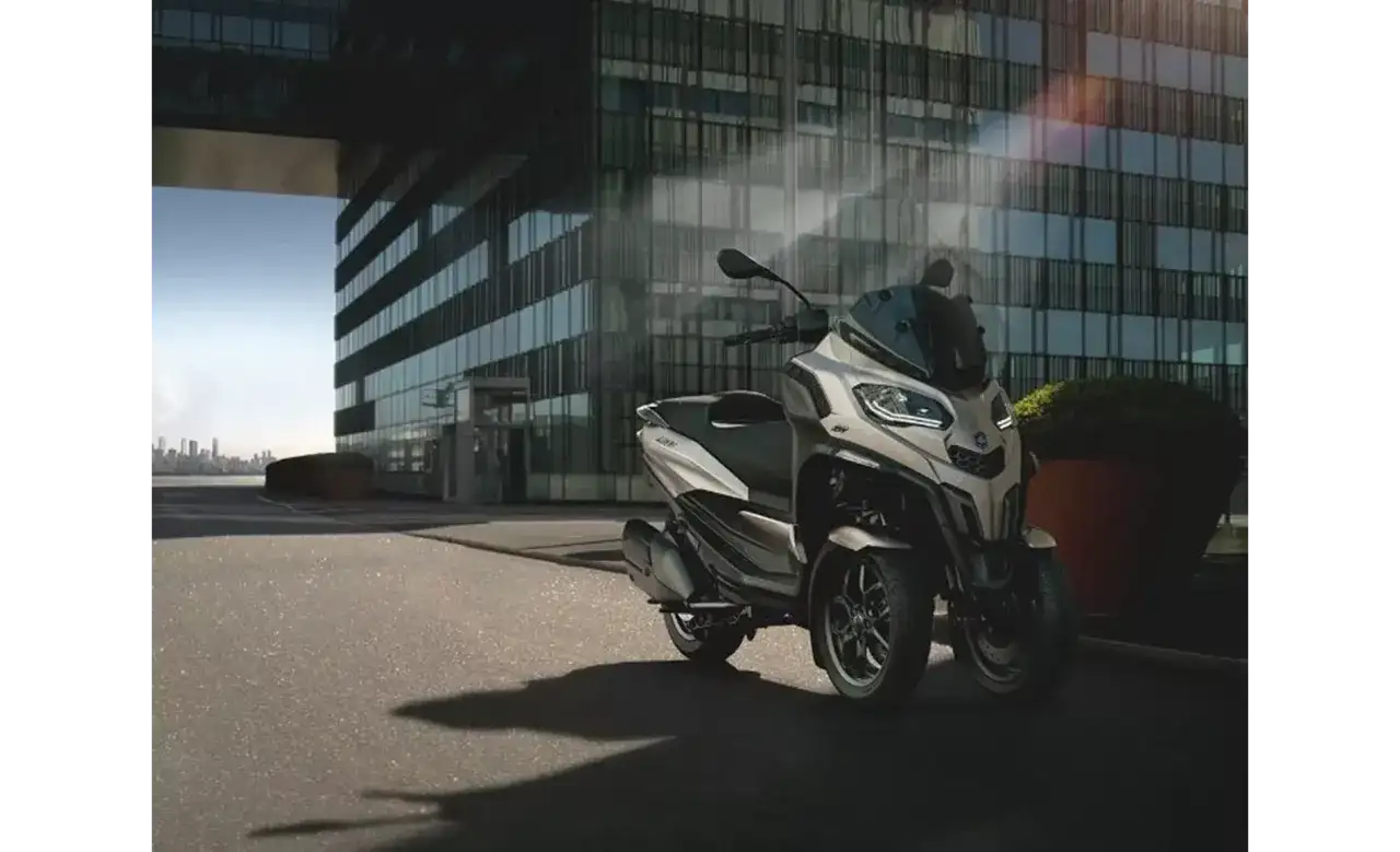 Nowoczesny Piaggio MP3, czy wersja 400 czy 500, parkuje przed szklanym budynkiem.