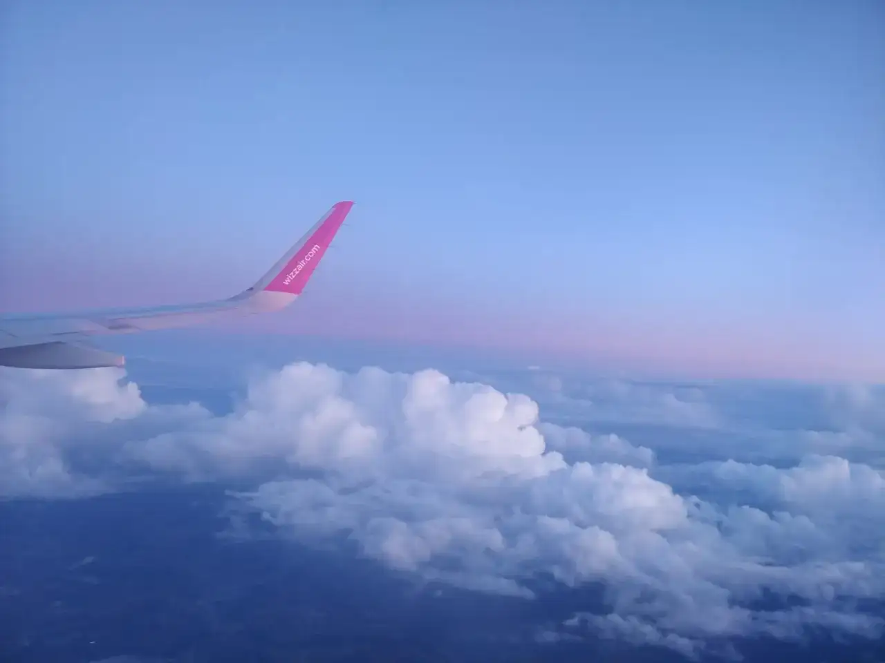 Skrzydło samolotu Wizz Air nad chmurami, wczesny poranek. Czas na loty do Anglii!