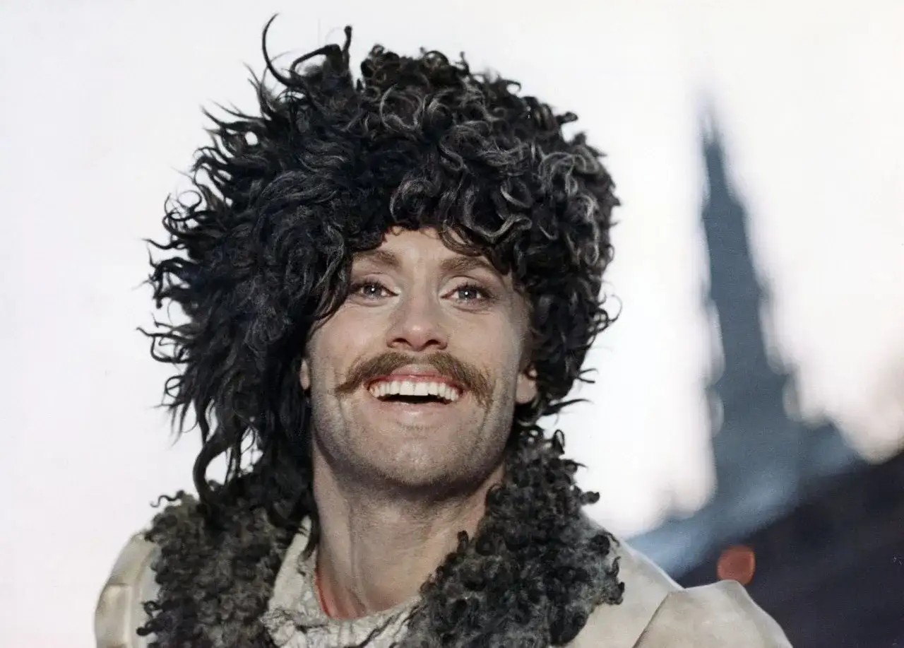 Daniel Olbrychski w filmach, z charakterystyczną burzą loków i wąsami, uśmiecha się szeroko.