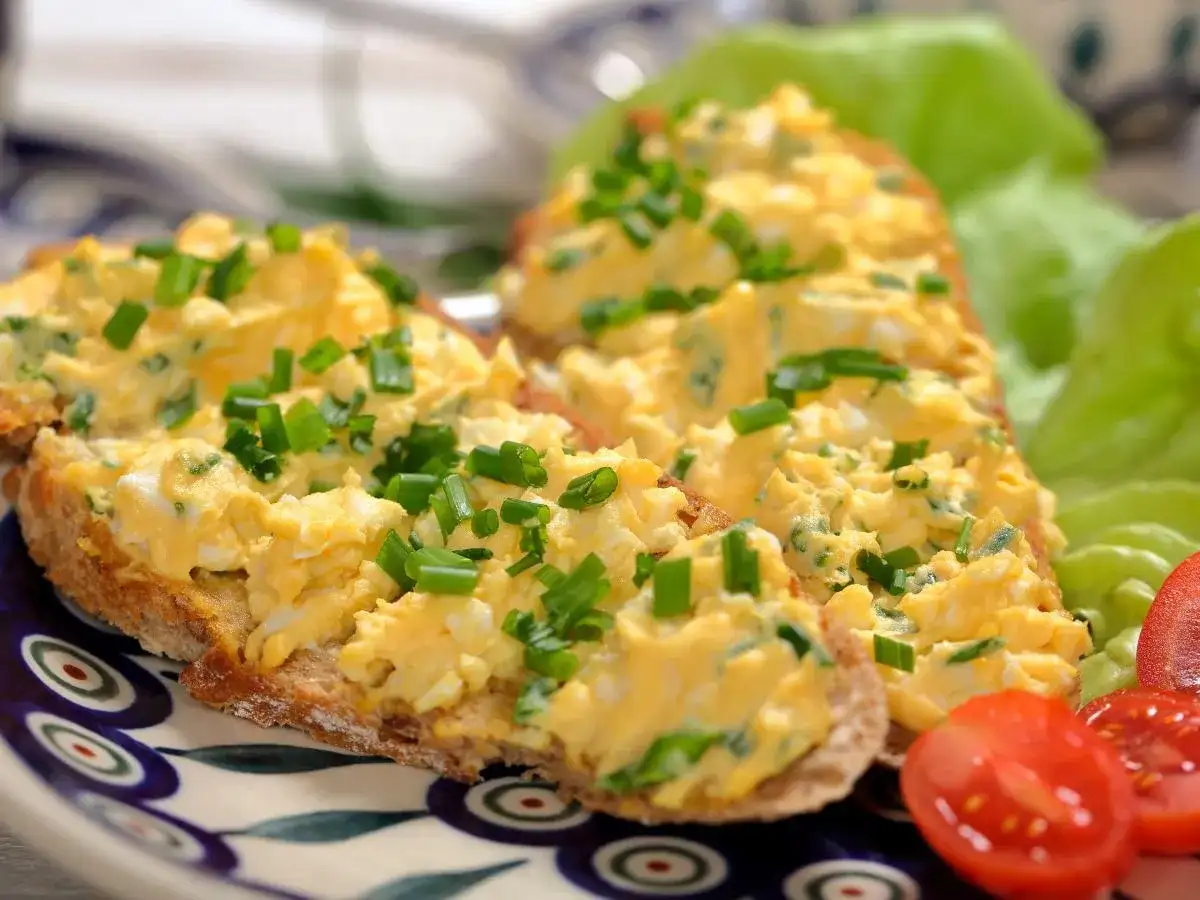 Pyszna pasta jajeczna jak dawniej, na chlebie, posypana szczypiorkiem. Obok sałata i pomidorki.