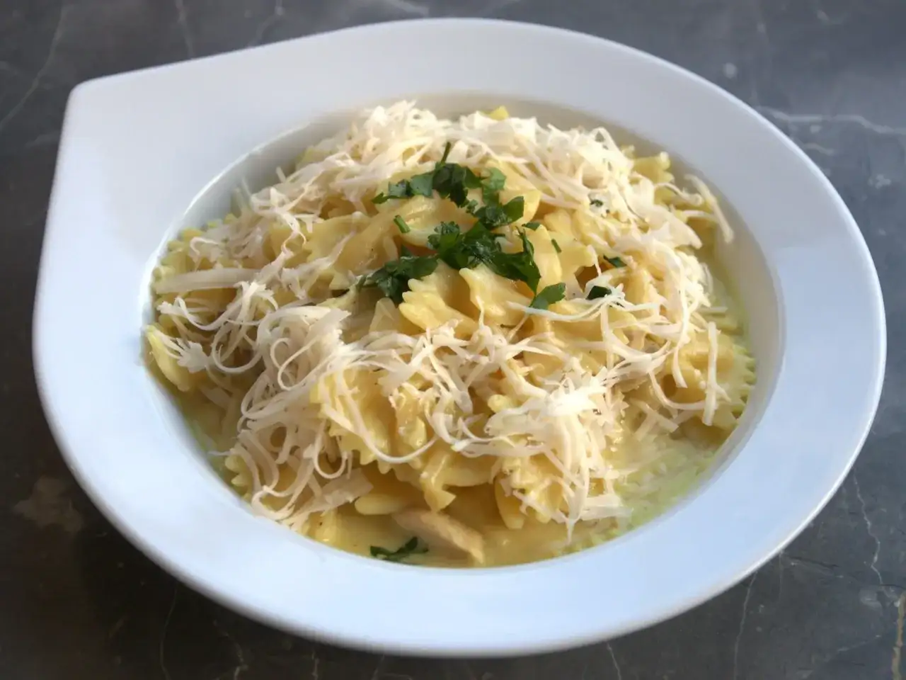 Szybki obiad z twarogiem: makaron farfalle w kremowym sosie, posypany startym serem i natką pietruszki.