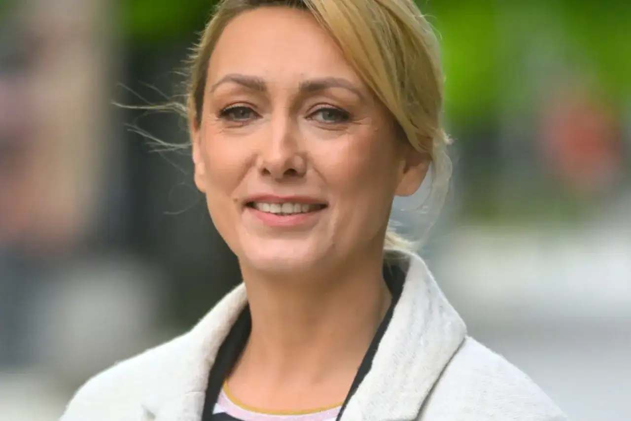 Portret uśmiechniętej blondynki w jasnym płaszczu.
