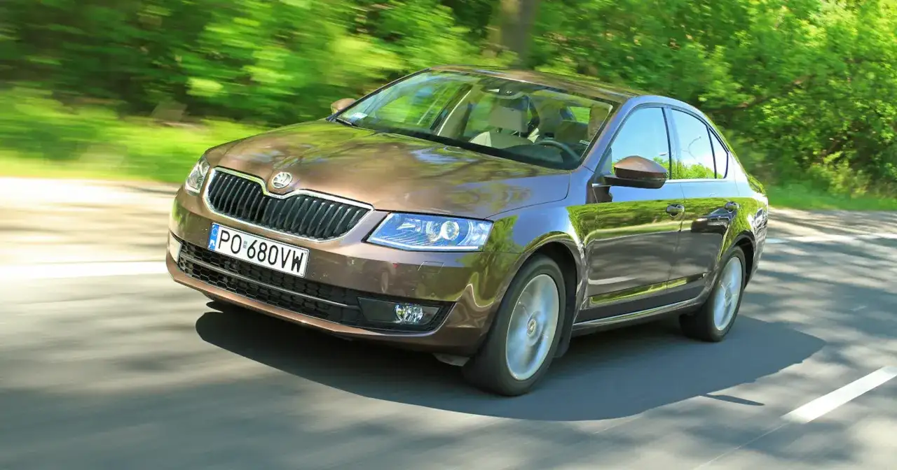 Brązowa Skoda Octavia jedzie po drodze wśród zieleni. Sprawdź aktualną skoda octavia cena!