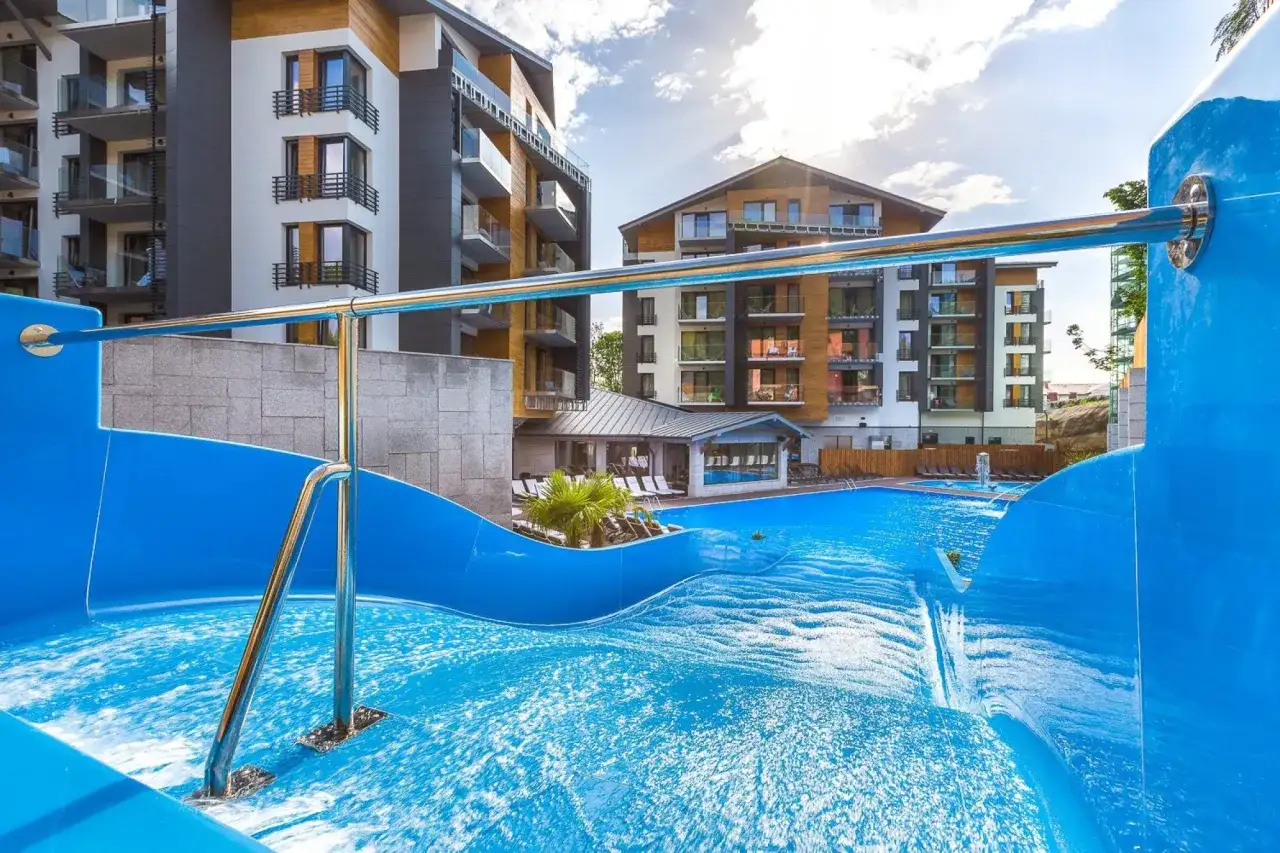 Basen z falą i zjeżdżalnią w hotelu Blue Mountain w Szklarskiej Porębie. Nowoczesne budynki hotelowe w tle.