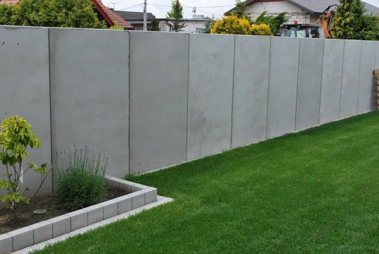 Nowy, wysoki betonowy płot dzieli działki, symbolizując konflikt z sąsiadem o ogrodzenie.